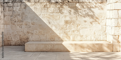 Minimalist Yucatan architecture featuring whitewashed stone walls with dramatic natural sunlight casting geometric shadows. Stone bench against textured wall creates clean lines and peaceful com photo