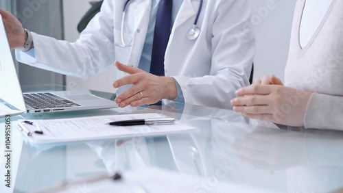 Doctor is consulting patient in modern fair clinic. Healthcare professional discusses medical information with a woman, pointing into the laptop computer monitor. Medicine concept photo