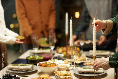 Cropped shot of woman lighting candlestick while serving festive dinner together with family on Christmas Eve, copy space photo