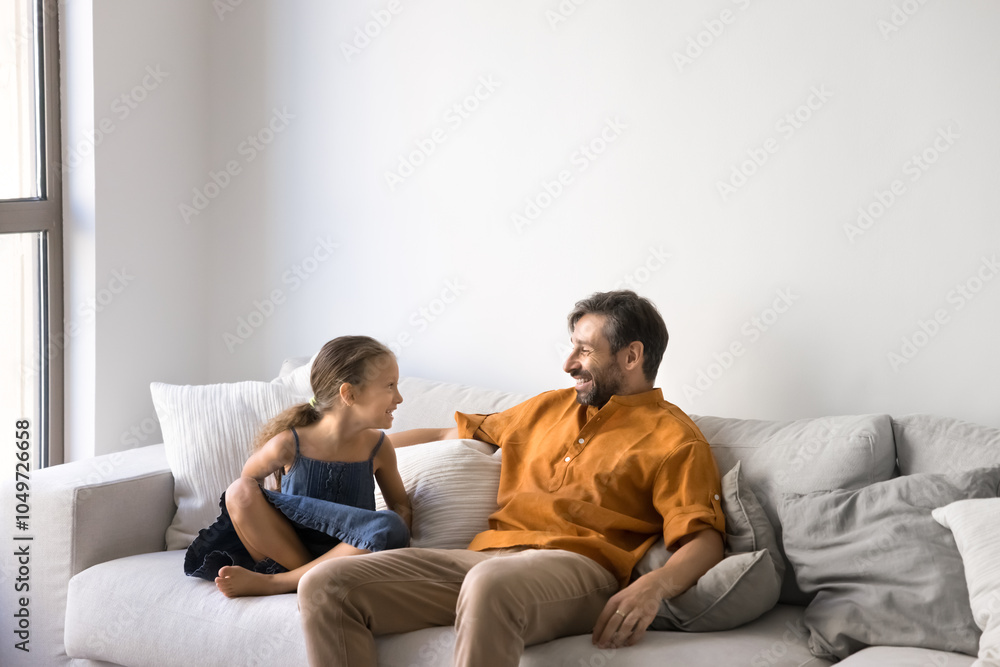 Positive sweet little kid girl and happy middle aged Latin father relaxing on home sofa, talking and laughing, chatting, having fun together, enjoying family leisure, fatherhood, childhood Positive sweet little kid girl and happy middle aged Latin father relaxing on home sofa, talking and laughing, chatting, having fun together, enjoying family leisure, fatherhood, childhood