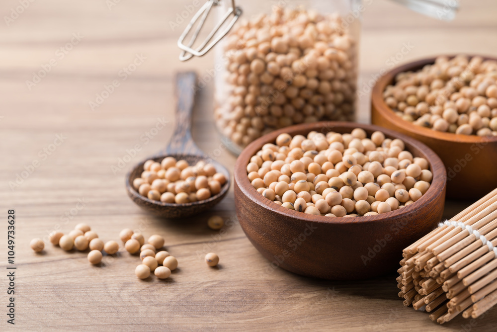 Fototapeta premium Soy bean seeds in wooden bowl, glass jar and spoon on wooden background