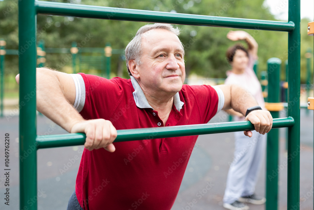 Obraz premium Elderly man doing leg stretching on the outdoor sports ground