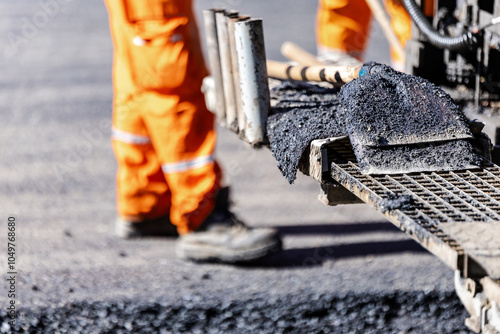 Construction worker operating an asphalt paving machine on a roadway in broad daylight, laying down fresh pavement photo