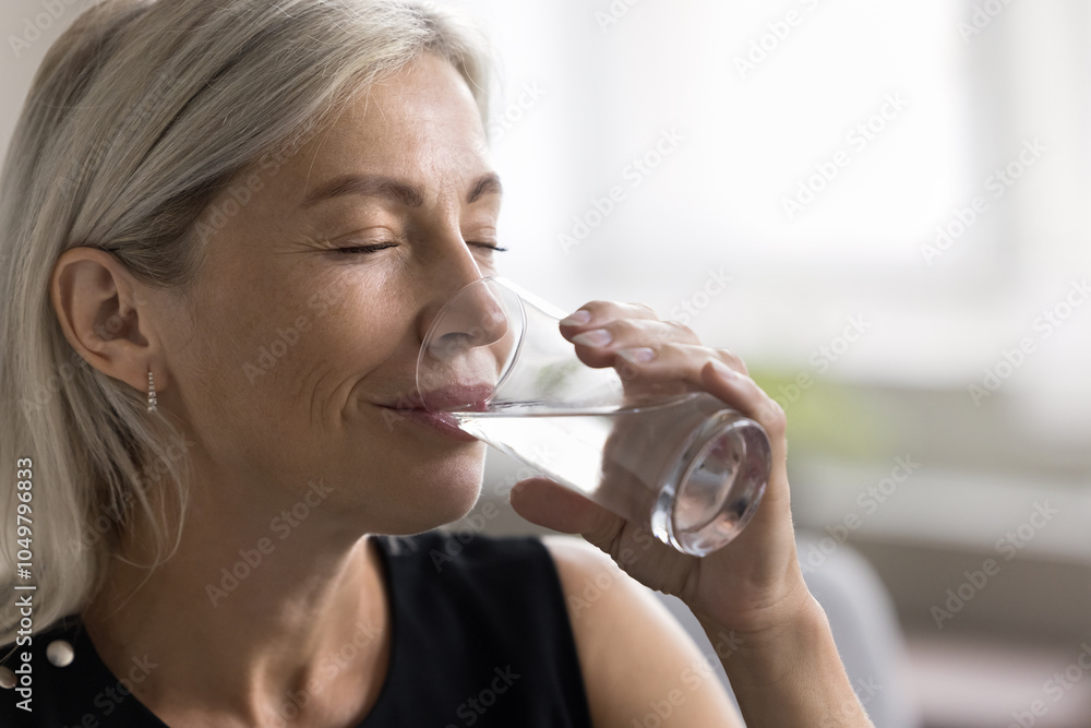 © fizkes - Smiling face of elderly lady relieving stress having glass of natural cold filtered water in dry hot summer day. Mature woman has healthy habit for easy skin body care hydrating drink enjoy every sip