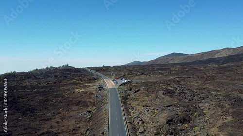 Drone / Aerial view of a road cutting through ancient volcanic lava fields on Tenerife, showcasing a rugged volcanic landscape under a clear blue sky