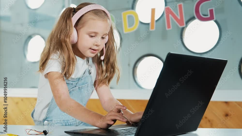 Young student working on laptop or studying in online classroom. Caucasian girl typing on laptop while doing homework or listening music. Little kid wearing headphone. Creative learning. Erudition. Young student working on laptop or studying in online classroom. Caucasian girl typing on laptop while doing homework or listening music. Little kid wearing headphone. Creative learning. Erudition.
