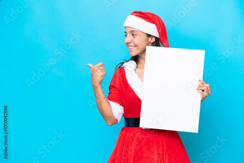 Young hispanic woman dressed as mama noel isolated on white background holding an empty placard and pointing side photo