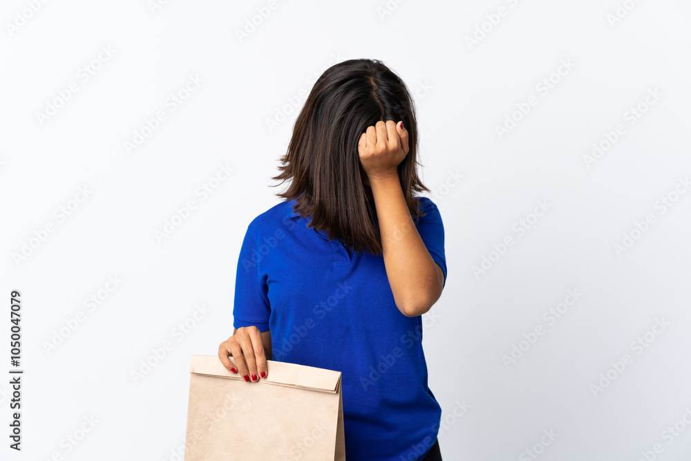 Young latin woman holding a grocery shopping bag isolated on white background with headache Young latin woman holding a grocery shopping bag isolated on white background with headache
