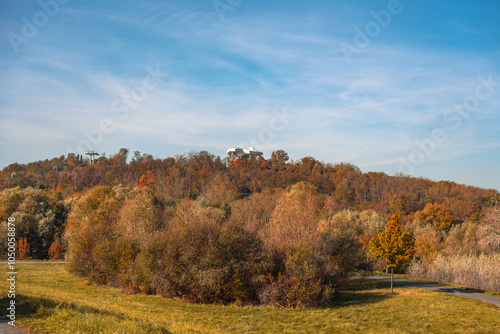 A beautiful autumn day with a view of a hill covered in trees. The trees are mostly brown and orange, and the sky is clear and blue photo