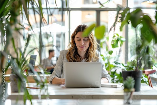 A professional woman is focused on her laptop in a vibrant, plant-filled cafe setting, creating a modern workspace vibe enhanced by warm light and aesthetics.