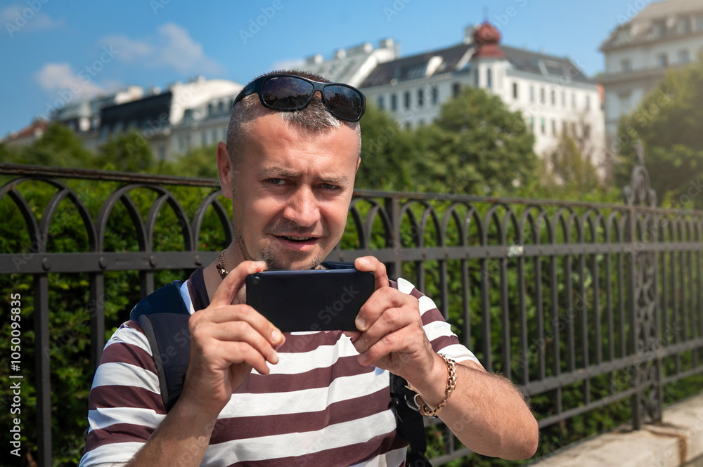 Fototapeta premium Male tourist taking photos on phone in the city. Young man takes a selfie with his smart phone.