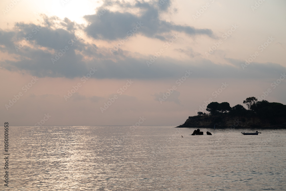 Early morning scene in Greece, with tranquil sea and a boat moored in silouette close to a cape cod peninsula with cumulus clouds in the sky. Early morning scene in Greece, with tranquil sea and a boat moored in silouette close to a cape cod peninsula with cumulus clouds in the sky.