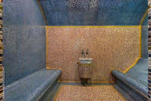 The interior of the Turkish bath hamam, decorated with beige and blue mosaic tiles. Wide benches and a shaped sink. photo