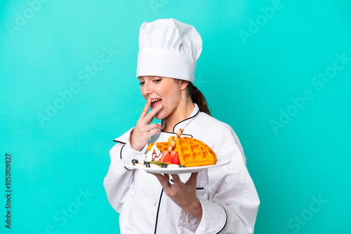 Young caucasian chef woman holding waffles isolated on blue background with surprise and shocked facial expression photo