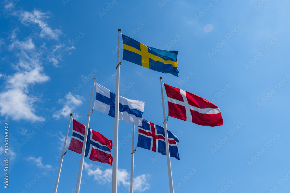 Scandinavian countries flags waving on metal poles against blue sky.