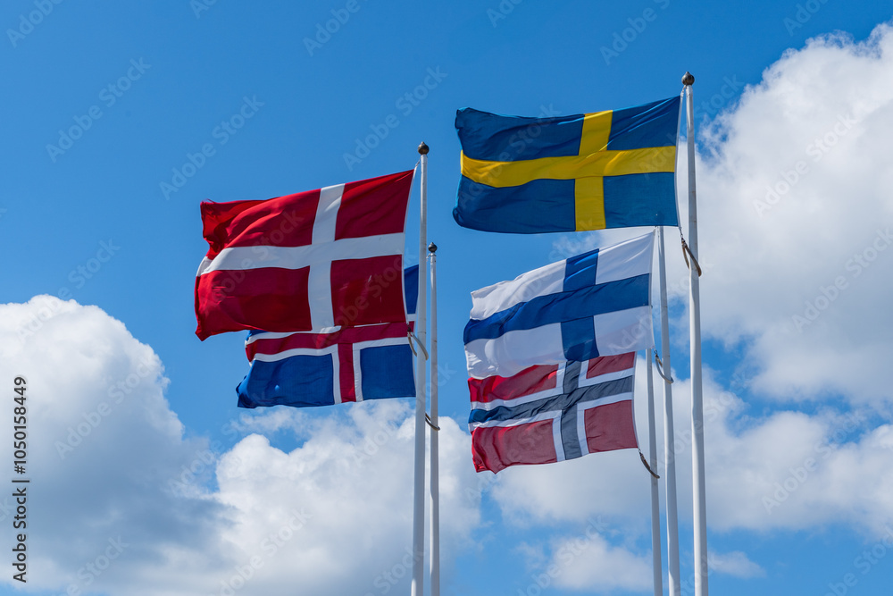 Scandinavian countries flags waving on metal poles against blue sky.