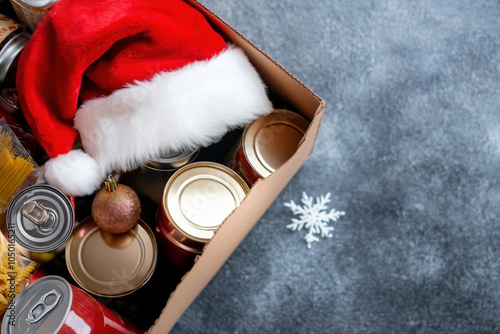 Christmas donation, charity, food bank, help for low income, poor families, homeless people. Cardboard box full of grocery products and Christmas Santa hat on gray background. Top view photo