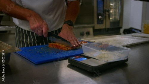 Professional chef cuts up and weighs fish as he prepares food in a professional kitchen