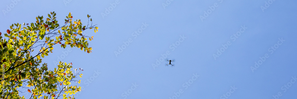 A drone hovers in a clear blue sky next to autumn leaves, symbolizing modern technology and seasonal change A drone hovers in a clear blue sky next to autumn leaves, symbolizing modern technology and seasonal change