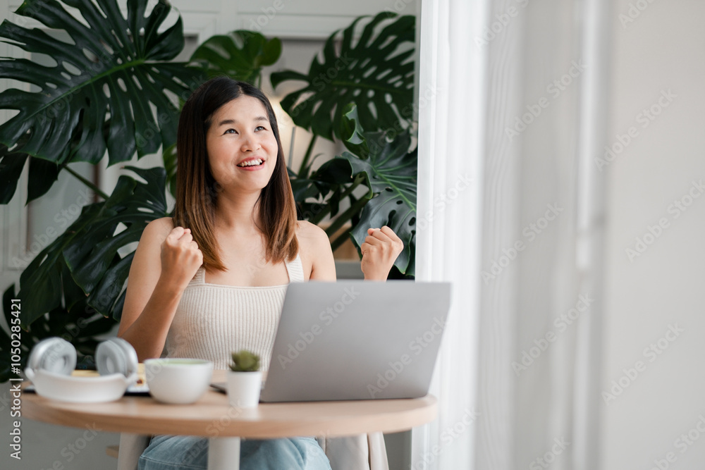 Happy woman celebrating success while working on a laptop at a cozy home office with plants. Happy woman celebrating success while working on a laptop at a cozy home office with plants.