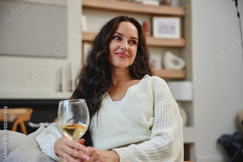 Woman enjoys a glass of white wine while relaxing at home in evening light