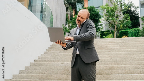 A business man near a modern business center is holding a laptop and talking on the phone. Business and modern technology concept.