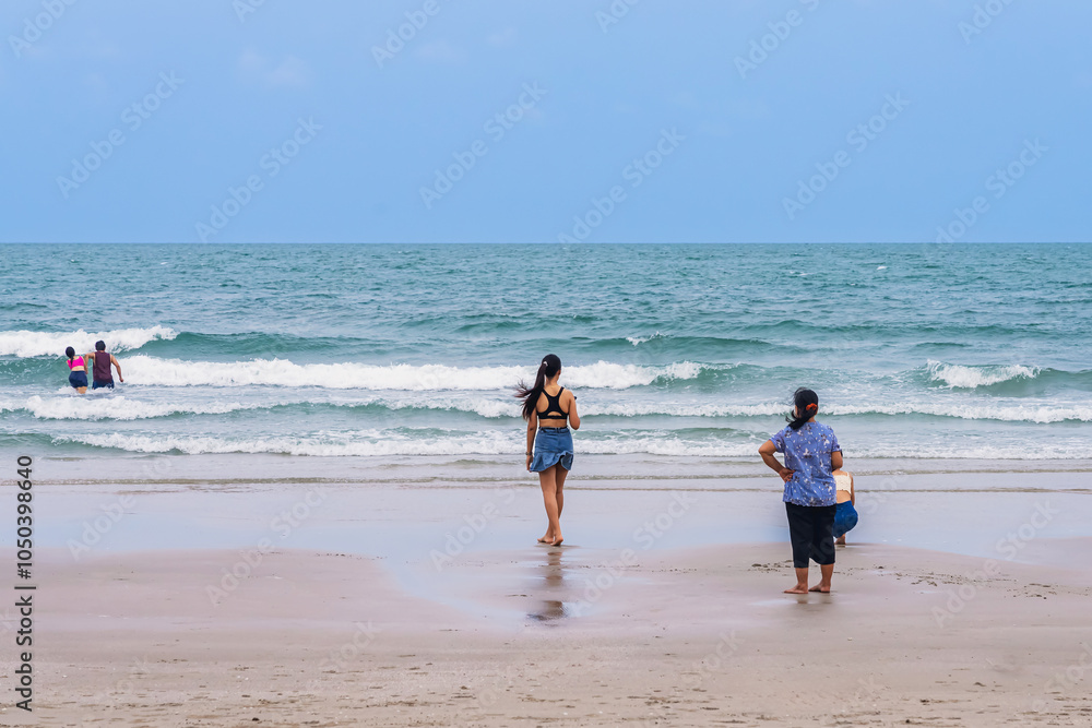 Back view of happy carefree woman using mobile phone at beach. Woman using smartphone standing at beach. Beautiful lovely young woman spending time at beach. Concept of travel, tourism and vacation.