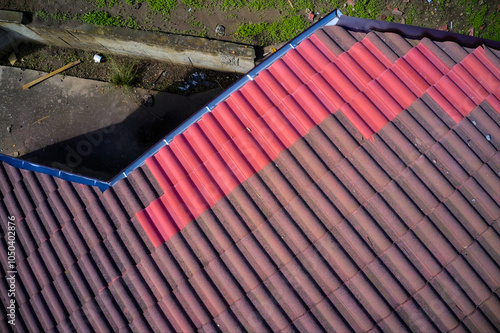 Фотография Aerial view of a tiled roof after partial repairs, showcasing replaced tiles and an inspection following the renovation