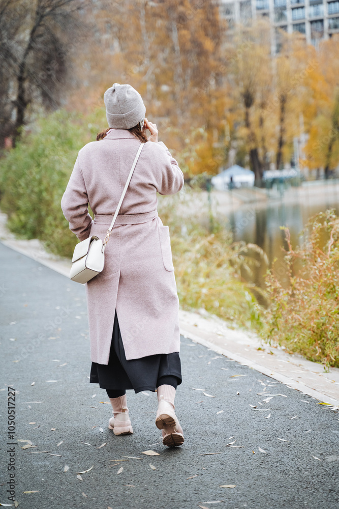 Obraz premium A woman dressed in a stylish pink coat and a matching hat is leisurely walking down a wellmarked path surrounded by various plants and trees, enjoying her stroll in the fresh air