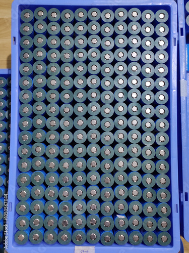 A top-down view of a blue plastic tray filled with cylindrical lithium-ion batteries arranged in a neat grid. Each silver-cased battery shows its black top and blue base, positive terminal up. photo