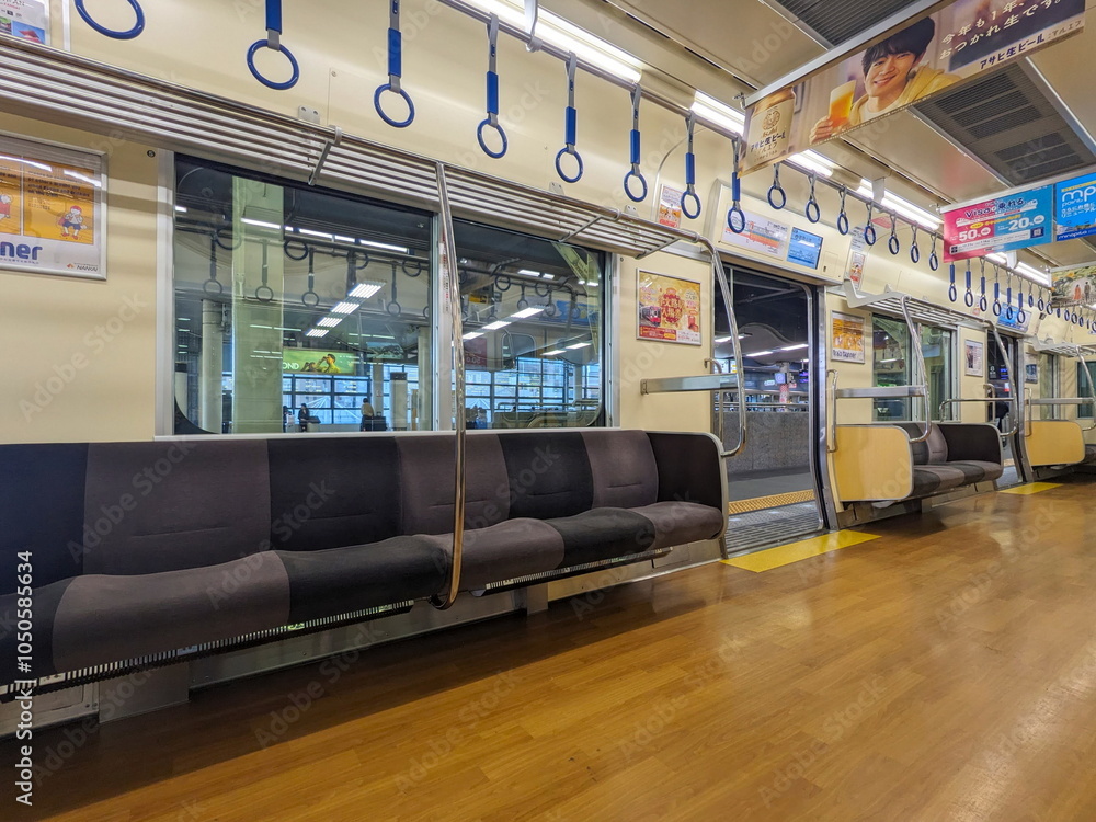 Obraz premium Osaka, Japan - 01.01.2024: Interior of a women-only carriage of Nankai Railway train with empty seats, hanging handrails, windows, and advertisement when stopped at Namba Station (Nankai)