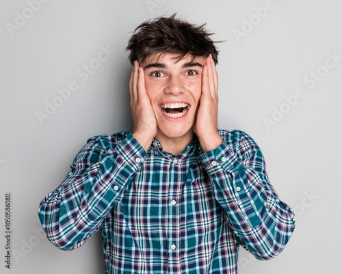 surprised young man covering temples with palms and laughing