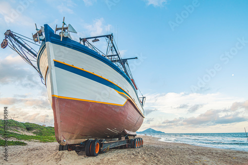 This photograph, taken on October 25, 2024, showcases a boat anchored in the sand of Navegantes, SC, Brazil, during a serene late afternoon. The setting sun
