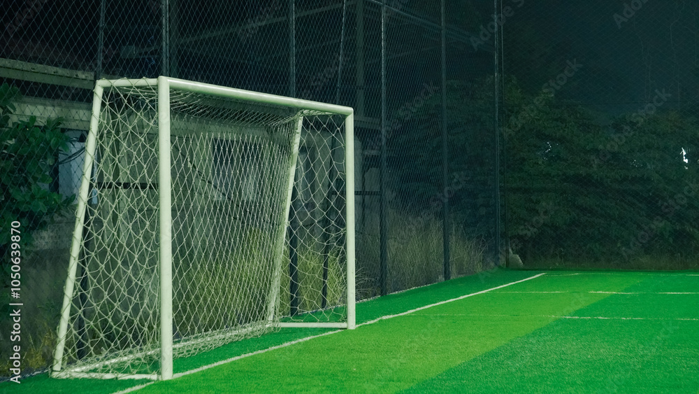 Fototapeta premium A soccer field at night with a goal in the center, illuminated by lamp posts
