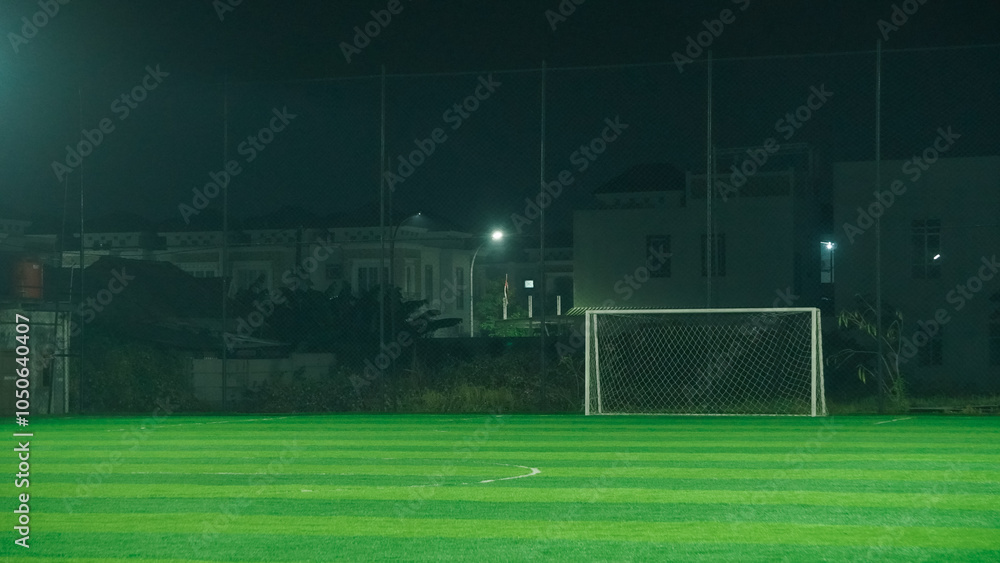 Fototapeta premium A soccer field at night with a goal in the center, illuminated by lamp posts