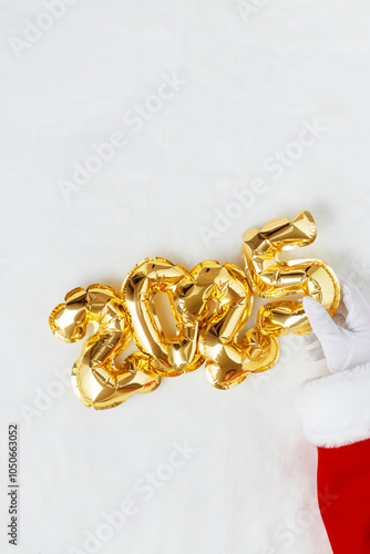 Canvas Print Santa's gloved hand holding gold foil balloons number 2025 on white fur backgrou