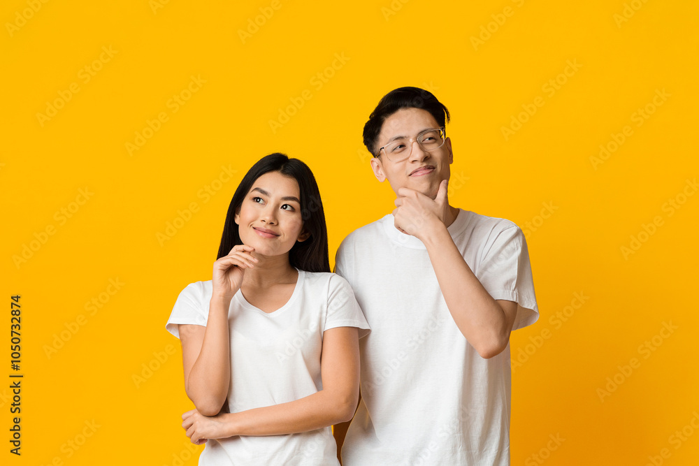 Planning future together. Young asian couple day dreaming on yellow studio background Planning future together. Young asian couple day dreaming on yellow studio background