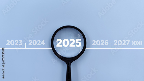 2025 inside of Magnifying glass in between previous and next year on blue background. Focus current year, achievement, target concept
