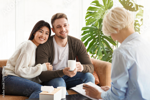 Adoption Counseling. Cheerful Young Couple Talking With Family Psychologist Sitting On Couch In Office. Selective Focus photo