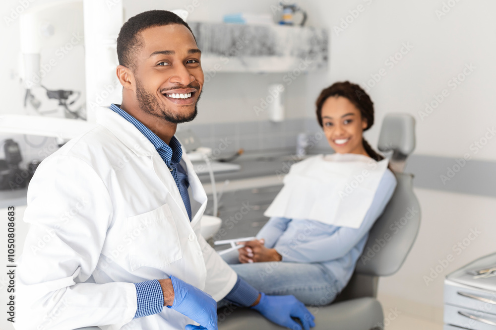 Obraz premium Visiting dentist. Black dentist doctor and female patient in chair smiling at camera, clinic interior