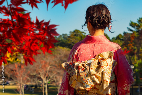 Japanese geisha with her back to camera. Girl is standing near red glue. Geisha admires oriental nature. Lady in traditional Japanese clothes. Geisha from Japan in national park. Woman in pink kimano photo