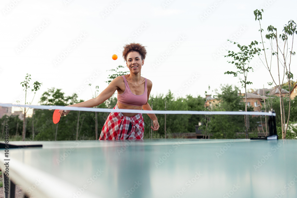 Fototapeta premium young african american girl playing table tennis outdoors in the park, woman hitting the ball with a ping pong racket