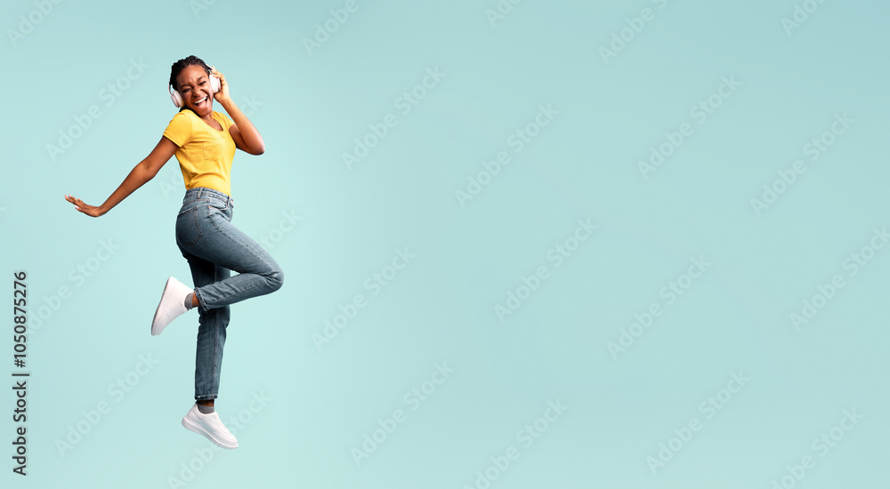 Music App. African Lady In Earphones Jumping Singing Favorite Song Having Fun In Studio Over Blue Background. Free Space Music App. African Lady In Earphones Jumping Singing Favorite Song Having Fun In Studio Over Blue Background. Free Space
