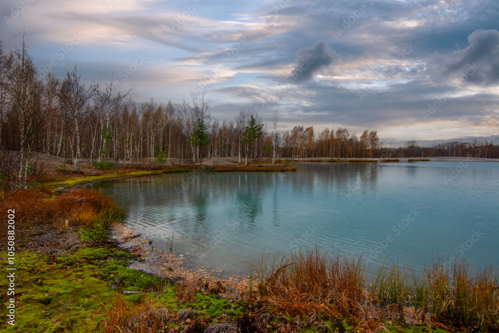 Autumn landscape A picturesque lake surrounded by trees in the background under a cloudy sky Autumn landscape A picturesque lake surrounded by trees in the background under a cloudy sky