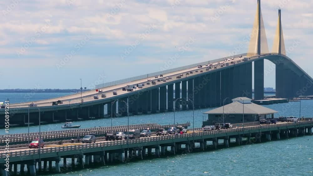 Sunshine Skyway Bridge over Tampa Bay in St Petersburg in Florida with fishing pier and driving traffic cars. Transportation infrastructure in USA Sunshine Skyway Bridge over Tampa Bay in St Petersburg in Florida with fishing pier and driving traffic cars. Transportation infrastructure in USA