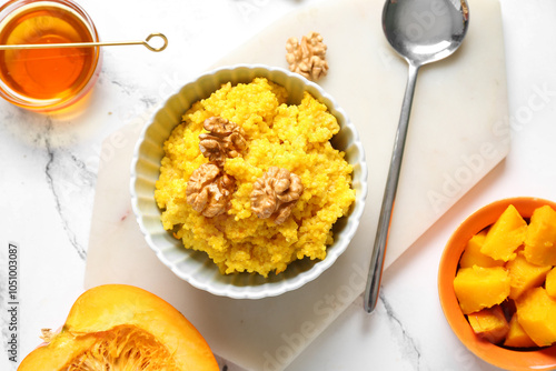 Bowl of tasty millet porridge with pumpkin, honey and nuts on white marble background