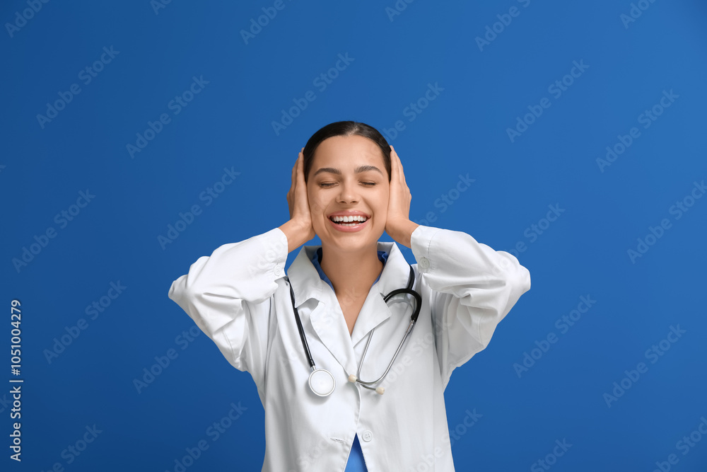 Beautiful young female doctor laughing on blue background Beautiful young female doctor laughing on blue background