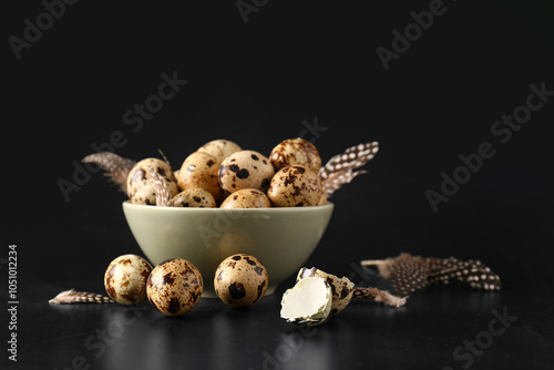 Bowl with fresh quail eggs and feathers on black background