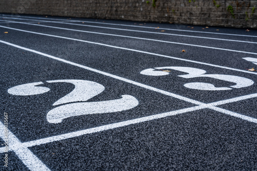 Close up lane number 2 on a new black running track with white lane lines and other markings. 