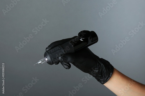 Professional cosmetologist holding permanent makeup machine on grey background, closeup photo